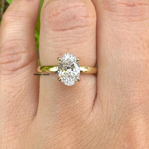 Puede incluir: Un anillo de compromiso de banda dorada con un gran diamante de forma ovalada.
