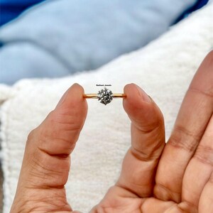 Puede incluir: Un anillo de compromiso de banda dorada con un diamante redondo y claro.