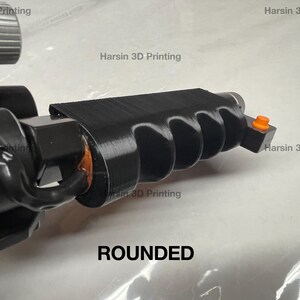 May include: A black 3D printed object with a rounded, textured surface and a small orange button. The object is labeled "ROUNDED".