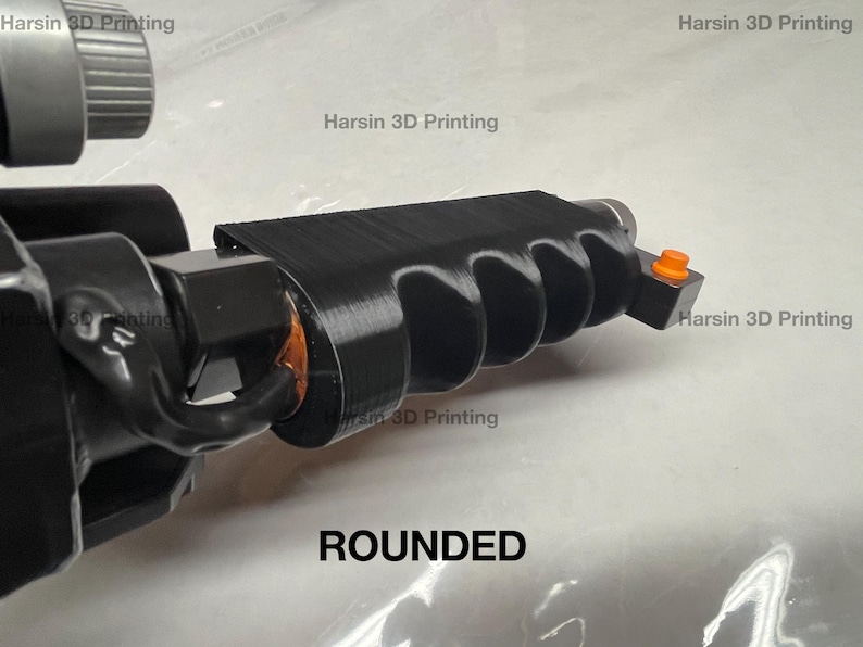 May include: A black 3D printed object with a rounded, textured surface and a small orange button. The object is labeled "ROUNDED".