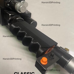 May include: A black plastic toy gun with an orange button and the word "CLASSIC" printed on the bottom. The gun has a textured grip and a silver barrel.