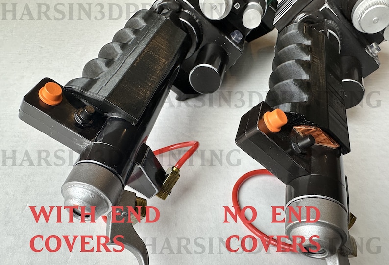 May include: Two black and silver 3D printed prop replicas of a fictional weapon. The replica on the left has a silver end cap, while the replica on the right has a raw, unfinished end. Both replicas have orange buttons and red tubing.