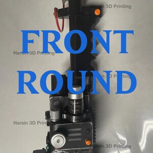 May include: A black and silver 3D printed prop replica of a Ghostbusters proton pack. The pack has a black handle, a silver top, and a black and silver body with various buttons and dials. The pack is labeled "LIPPARD" and "SLO-BLO".