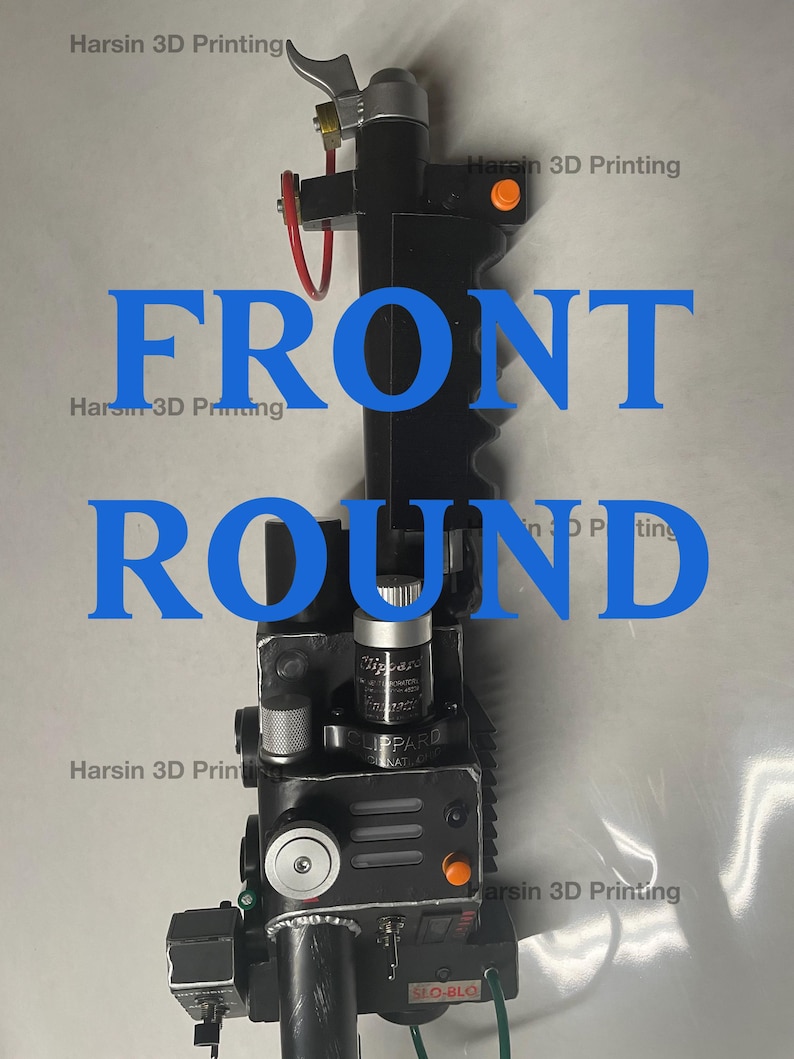 May include: A black and silver 3D printed prop replica of a Ghostbusters proton pack. The pack has a black handle, a silver top, and a black and silver body with various buttons and dials. The pack is labeled "LIPPARD" and "SLO-BLO".