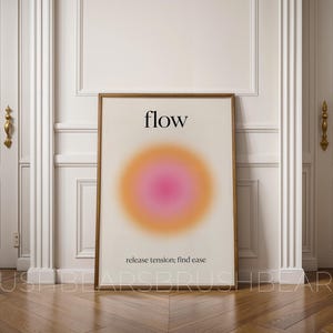 Puede incluir: Un cuadro enmarcado con la palabra "flow" en negro en la parte superior y un círculo degradado en tonos rosa y naranja. Debajo del círculo, el texto dice "release tension; find ease". El cuadro está en un marco de madera.