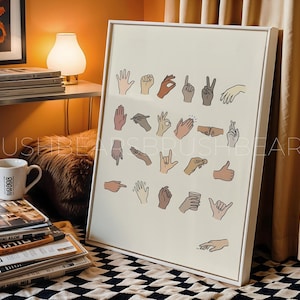 May include: A framed print featuring various hand gestures in different skin tones, set against a cream background. The artwork showcases a range of hand signs, including the peace sign, thumbs up, and others, in a minimalist style.