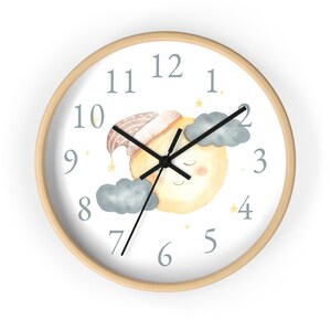 May include: A white wall clock with a wooden frame features a sleeping moon with a blue and brown hat, clouds, and stars. The clock face has gray numbers 1 through 12.