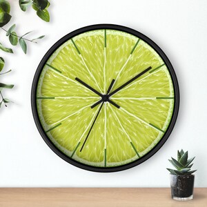 May include: A black framed clock with a lime slice design. The clock face is a close-up of a lime slice with a green rind and a yellow center.