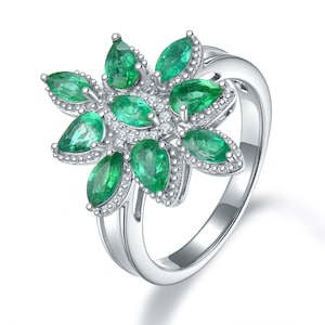 May include: A silver ring featuring a floral design with pear-shaped emeralds and small, round diamonds. The emeralds are a vibrant green, and the ring has a polished finish. The ring's band splits into two at the top, adding to its unique design.
