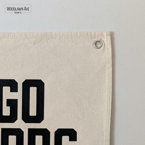 以下が含まれることがあります： 白いキャンバスのタペストリーに黒い文字で「GO DOC」と書いてあります。タペストリーの右上隅にはグロメットがあります。