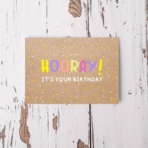 Könnte beinhalten: Eine braune Karte mit bunten Konfetti und dem Text "HOORAY! It's your birthday" in einer verspielten Schriftart.