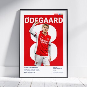 May include: Framed poster featuring Martin Ødegaard in an Arsenal jersey. The poster has a red background with a large white number 8. The player's name is at the top, and the Emirates logo is visible. Additional text includes player details.