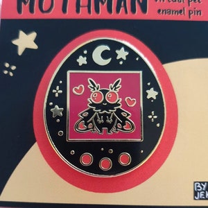Op de afbeelding: Emaille pin met een cartoon Mothman ontwerp. De pin heeft een zwarte achtergrond met een rode rand en gouden accenten. De Mothman is rood en zwart met hart details. De tekst "MOTHMAN virtual pet enamel pin" staat bovenaan.