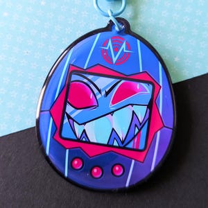 May include: A blue and purple keychain featuring a cartoon character with a menacing expression. The keychain has a blue clasp and a design reminiscent of a retro handheld game. The character has a red mouth and eyes.
