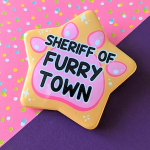 May include: A yellow star-shaped button with a pink paw print and the text "Sheriff of Furry Town".