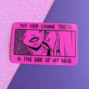 May include: A pink rectangular sticker with black text and a black and pink illustration. The text reads "PUT HER CANINE TEETH IN THE SIDE OF MY NECK". The illustration depicts two figures in a close embrace.