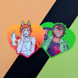 May include: Two heart-shaped stickers. One features a fox-like character with orange fur, a white top, and a playful expression. The other shows a person with a drill, wearing a green jacket and a sinister grin, with red splatters.