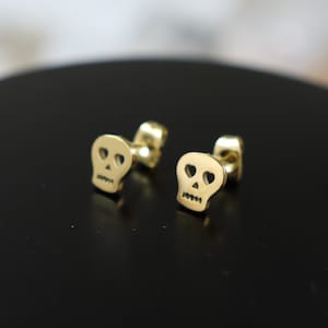 May include: A pair of gold-toned skull stud earrings with heart-shaped eye details.