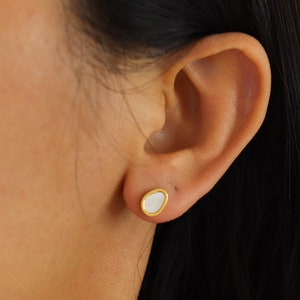 May include: A pair of gold oval-shaped earrings with a white center.