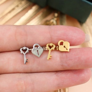 Puede incluir: Cuatro abalorios de plata y oro en forma de llave y candado. Los abalorios tienen forma de corazón con una cerradura y una llave. Los abalorios están en un dedo.