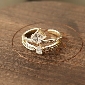 May include: A gold ring with two clear cubic zirconia stones. The larger stone is square shaped and the smaller stone is pear shaped.