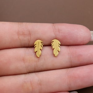 Puede incluir: Un par de pendientes de botón de plumas de color dorado.