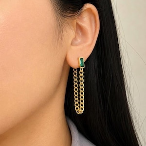 May include: A gold-tone earring featuring a rectangular emerald green gemstone stud connected to a dangling chain loop. The chain is attached to the base of the stud, creating a continuous drop design that hangs vertically from the earlobe.