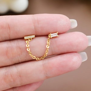 May include: Gold chain earrings with two clear cubic zirconia stones. The chain is connected to a bar with a cubic zirconia stone on each end.