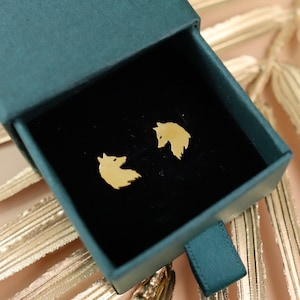 May include: A pair of gold fox head stud earrings in a green velvet box. The earrings are small and delicate, and they would make a great gift for someone who loves foxes.