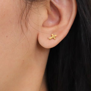 Puede incluir: Un par de pendientes de cruz de oro. Los pendientes son pequeños y delicados, y son perfectos para el uso diario.