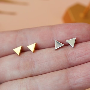 Könnte beinhalten: Ein Set mit drei Dreiecks-Ohrsteckern. Zwei Ohrstecker sind golden und ein Ohrstecker ist silber.