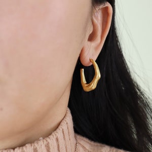 Könnte beinhalten: Goldene Creolen mit einem einzigartigen, strukturierten Design in Form einer Hand.