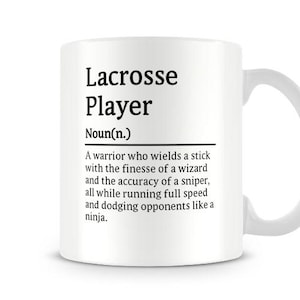 May include: White ceramic coffee mug with a black and white graphic design. The text reads "Lacrosse Player Noun(n.) A warrior who wields a stick with the finesse of a wizard and the accuracy of a sniper, all while running full speed and dodging opponents like a ninja."