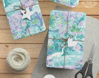May include: Two gift boxes wrapped in blue and purple floral patterned paper with white birds and waves. The boxes are tied with twine and have white paper tags attached. The boxes are on a wooden surface with a spool of twine and a pair of scissors.