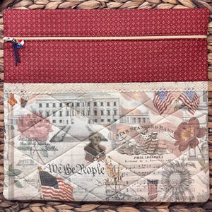 K&ouml;nnte beinhalten: Eine rechteckige Stofftasche mit einem oberen Teil aus rotem Stoff mit wei&szlig;en Punkten und einem unteren Teil mit gestepptem patriotischem Druck. Das Motiv zeigt das Wei&szlig;e Haus, amerikanische Flaggen, Blumen und den Text We the People.