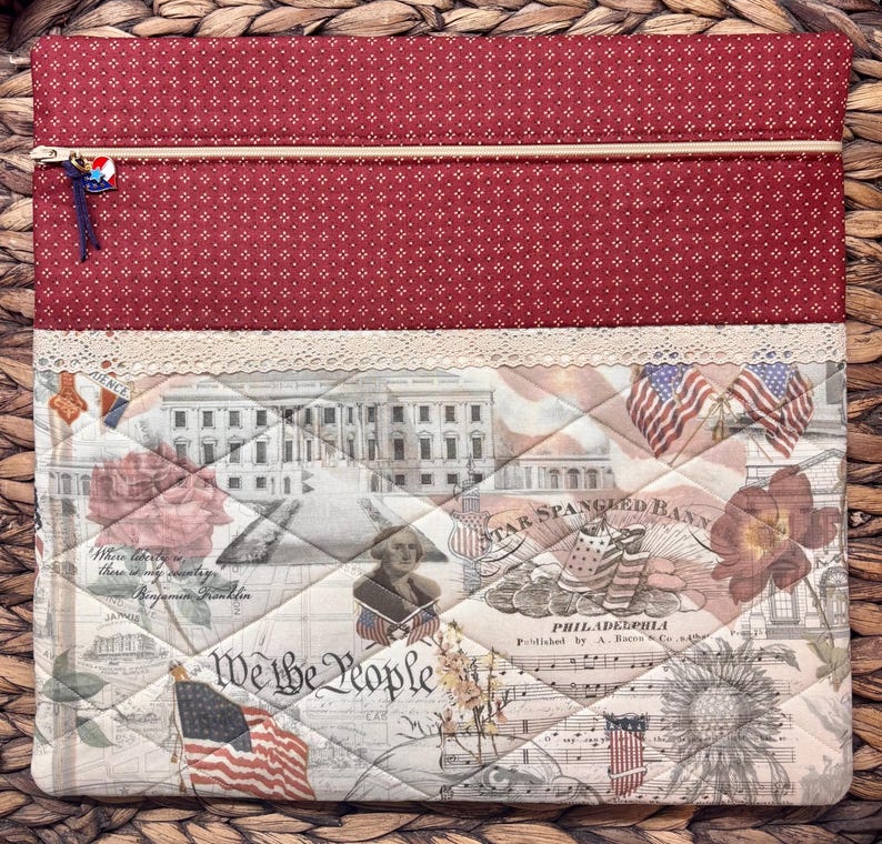 K&ouml;nnte beinhalten: Eine rechteckige Stofftasche mit einem oberen Teil aus rotem Stoff mit wei&szlig;en Punkten und einem unteren Teil mit gestepptem patriotischem Druck. Das Motiv zeigt das Wei&szlig;e Haus, amerikanische Flaggen, Blumen und den Text We the People.