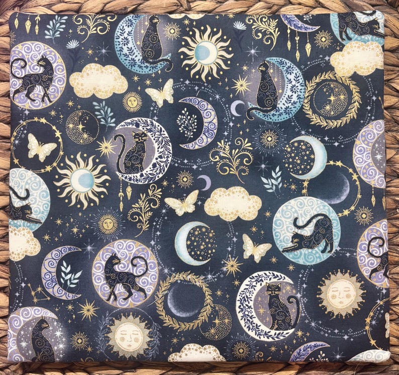 以下が含まれることがあります： 黒猫、月、太陽、蝶、星が描かれた、暗い青色の生地。 金色、白、ラベンダー色のアクセントがデザインに含まれています。 この生地は、キルトや工芸品に使用される可能性があります。
