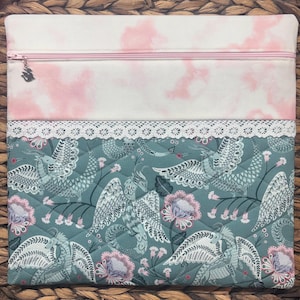 May include: A quilted fabric pouch with a pink zipper and a bird charm. The top section features a white fabric with pink cloud-like patterns. The bottom section has a teal background with a bird and floral design, and a white lace trim.