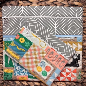 Può includere: Un set di pochette con cerniera in tessuto trapuntato. La pochette più grande è grigia con un motivo geometrico bianco. Le pochette più piccole presentano colorati disegni patchwork con motivi a tema cucito come bottoni, forbici e metro a nastro. Su sfondo intrecciato.