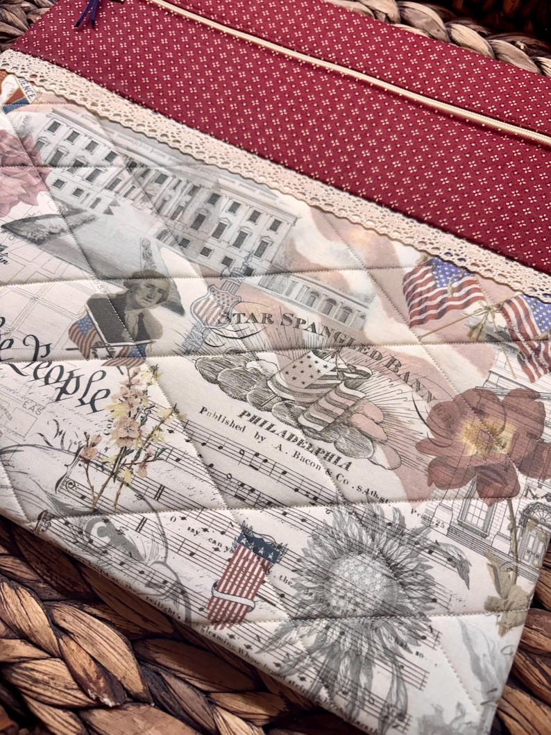 K&ouml;nnte beinhalten: Eine gesteppte Stofftasche mit einem patriotischen Aufdruck, der das Wei&szlig;e Haus, amerikanische Flaggen, Notenbl&auml;tter sowie den Text Star Spangled Banner und Philadelphia zeigt. Der obere Teil besteht aus rotem Stoff mit wei&szlig;en Punkten und einer cremefarbenen Spitzenborte.