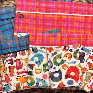 May include: Four zippered pouches with different patterns. The largest pouch is red and orange plaid. The other three pouches are smaller and feature a white background with colorful animal illustrations.