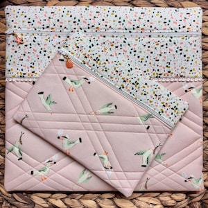 Könnte beinhalten: Ein Set aus gesteppten Stoffbeuteln. Die größere Tasche hat ein weißes Terrazzo-Muster mit Reißverschluss und einem Seestern-Anhänger. Die kleinere Tasche ist rosa mit einem Möwenmuster und einem Reißverschluss. Beide Taschen sind gesteppt.