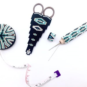 May include: A set of sewing tools with a beaded design. The set includes a pair of scissors, a needle threader, a thimble, and a tape measure. The tools are all black and white with turquoise accents.