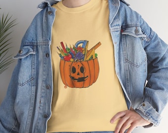 Könnte beinhalten: Ein gelbes T-Shirt mit einem Aufdruck einer mit Schulutensilien gefüllten Kürbis, darunter Bleistifte, Lineale und ein Geodreieck.