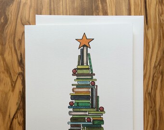 May include: A white greeting card with a Christmas tree design made of stacked books. The books are various colors, topped with an orange star and red ornaments. A white envelope is included.