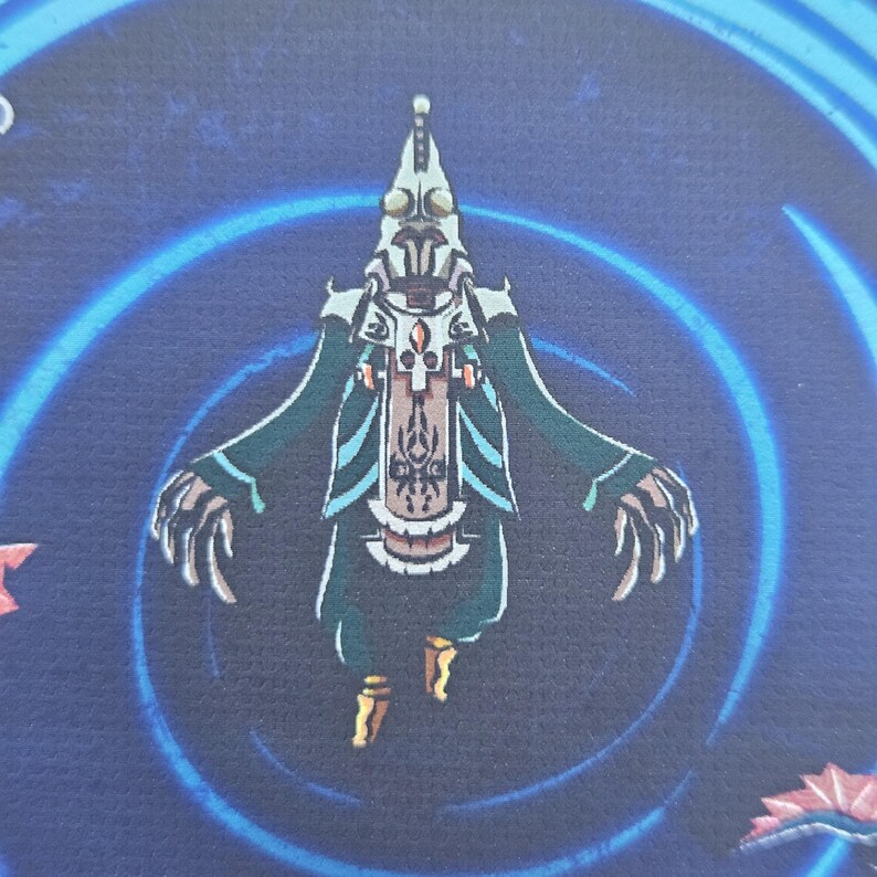 Puede incluir: Una ilustraci&oacute;n gr&aacute;fica de una figura humanoide con cabeza blanca puntiaguda, t&uacute;nicas verde oscuro y manos largas con garras. La figura est&aacute; centrada sobre un fondo azul oscuro con un patr&oacute;n circular azul claro y detalles en color rojo.