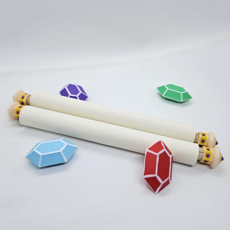 Puede incluir: Dos pergaminos cil&iacute;ndricos de color blanco roto con tapas de extremo de color tostado claro que presentan bandas amarillas y tachuelas moradas. Los pergaminos est&aacute;n rodeados por cuatro objetos facetados en forma de gema en morado, verde, azul claro y rojo, cada uno con contornos blancos.