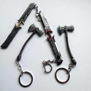 May include: Collection of miniature metal keychains featuring swords and hammers. The swords have intricate designs with gold or red accents. The hammers have detailed handles. Each keychain includes a ring for keys.