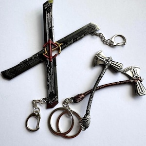 Puede incluir: Una colección de llaveros metálicos con diseños de una popular franquicia de superhéroes. Los llaveros incluyen un arma de doble filo y dos versiones de un martillo. Cada llavero tiene una cadena plateada y un cierre o anillo.
