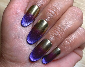 Uñas postizas con efecto ojo de gato morado: redondas medianas cromadas doradas en la foto.